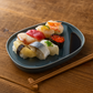 Assorted sushi on a dark blue plate with chopsticks on a wooden surface