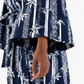 A close-up of a person wearing a navy blue and white patterned robe or kimono-style garment, with wide flared sleeves and a visible hand against a plain light background.