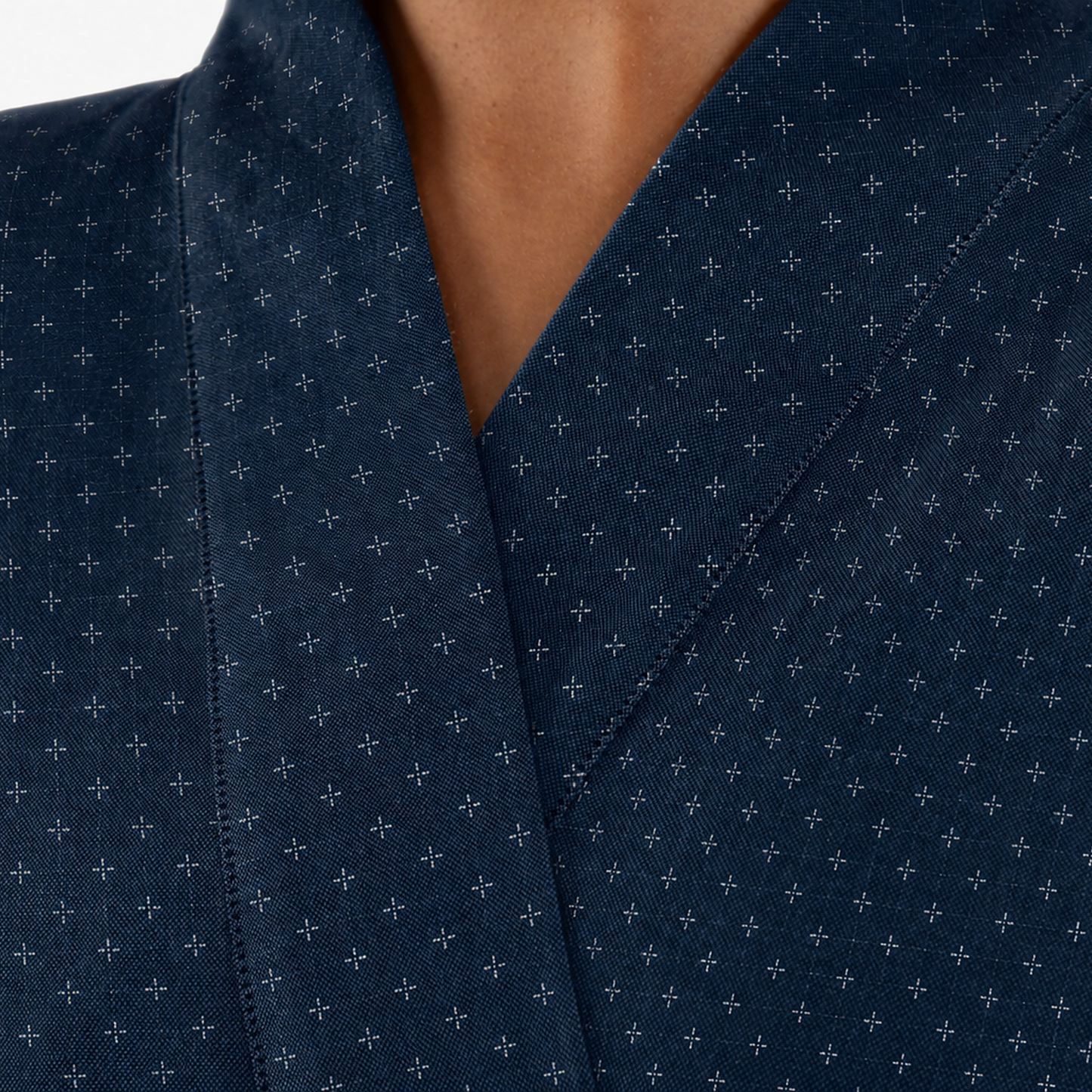 Close-up of a dark navy blue wrap-style garment with a small repeating white cross pattern, worn by a model.
