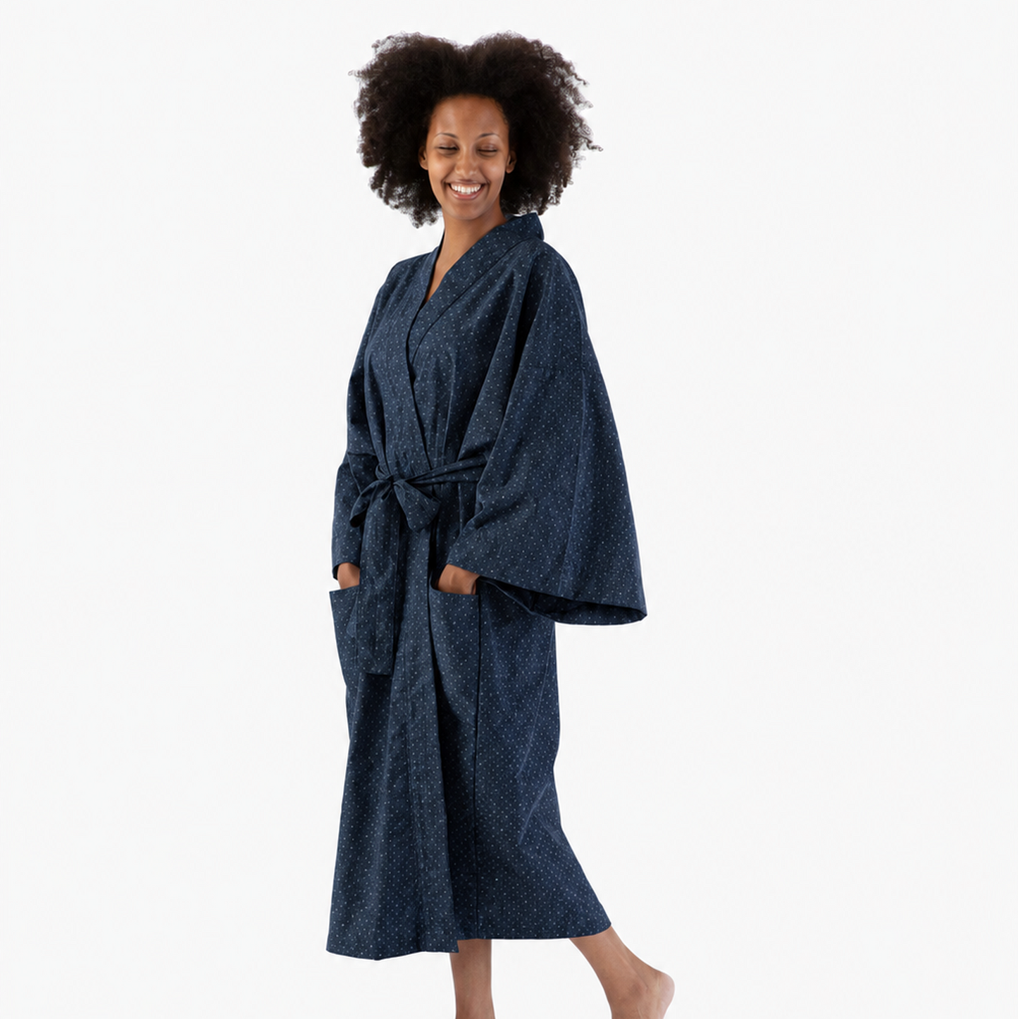 A smiling woman with curly dark hair models a dark navy blue patterned bathrobe against a plain white studio background.