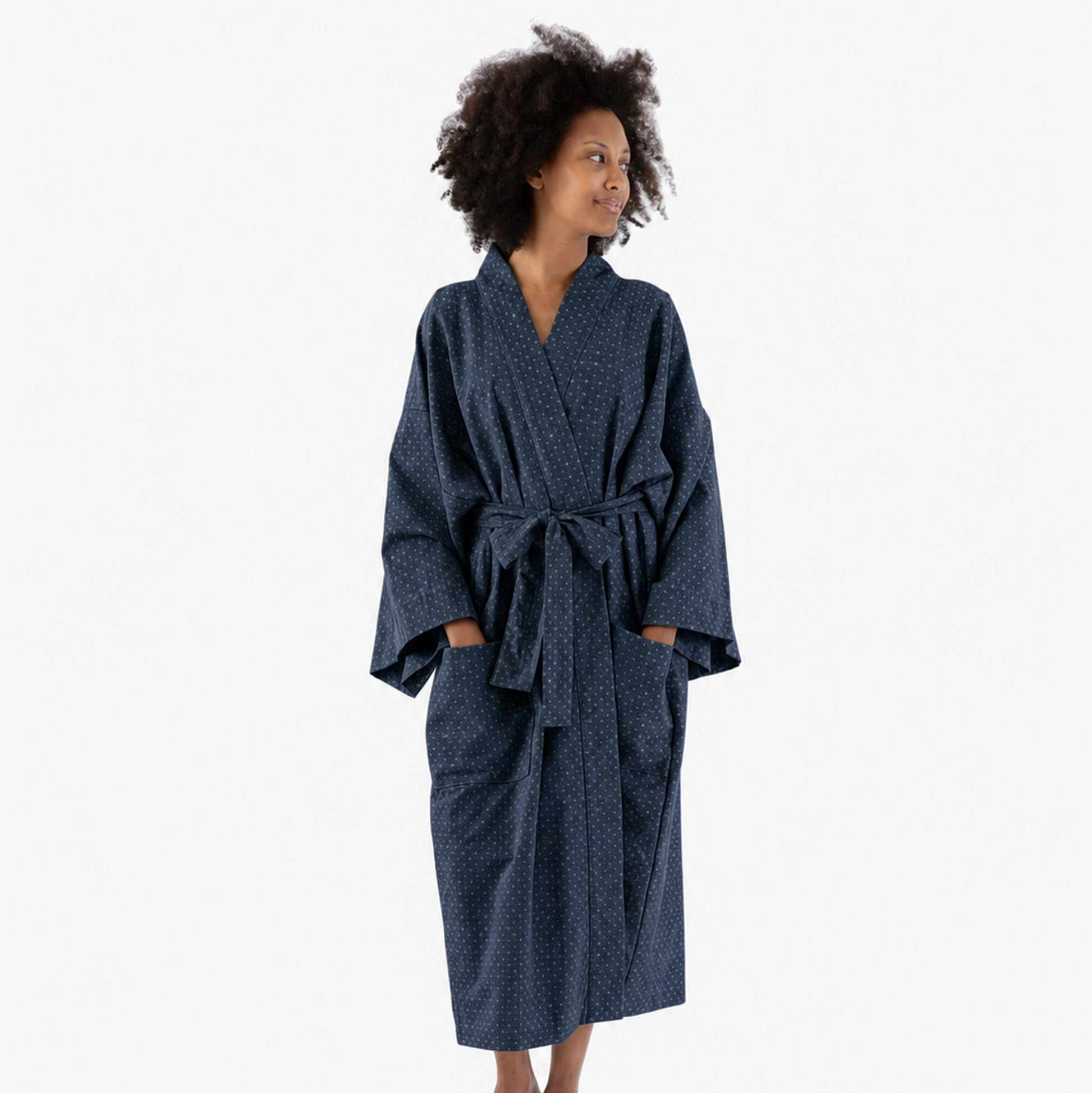 A woman wearing a dark navy blue patterned robe with a tie belt and front pockets, standing against a plain white studio background.