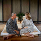 A man and a woman sitting on a low bed in a Japanese-style room, both wearing matching black and white patterned robes.