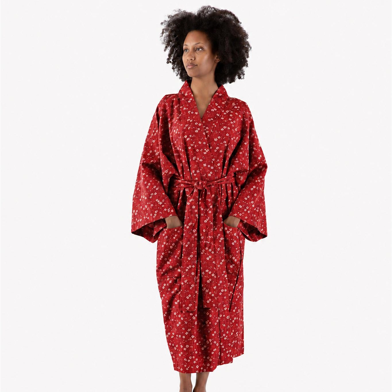 A woman wearing a red kimono-style robe with a white floral pattern, standing against a plain white studio background.