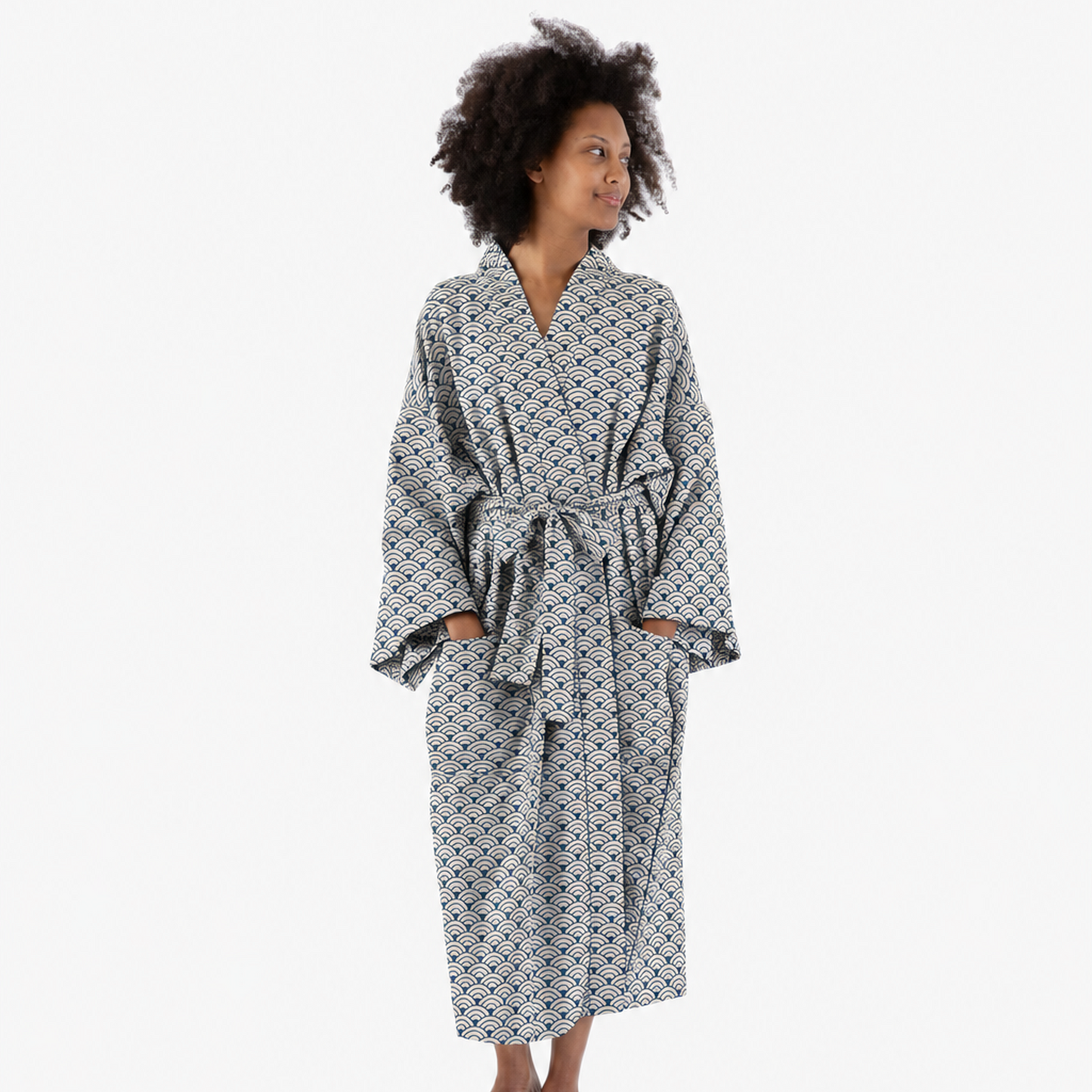 A woman wearing a long-sleeved, tie-front robe with a black and white geometric pattern, standing against a plain white studio background.