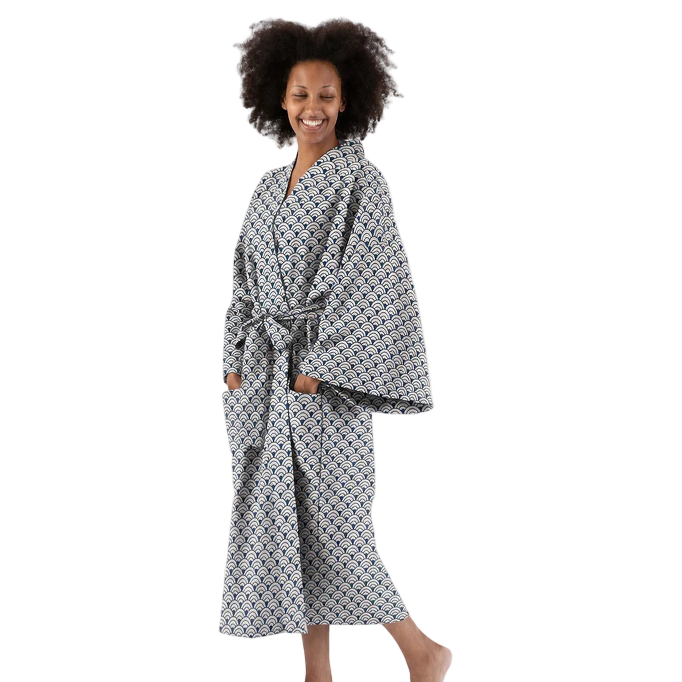 A woman wearing a long-sleeved patterned bathrobe with a matching waist tie, standing barefoot against a plain white studio background.
