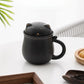 Black cat-shaped mug with a lid on a white surface with a plant in the background
