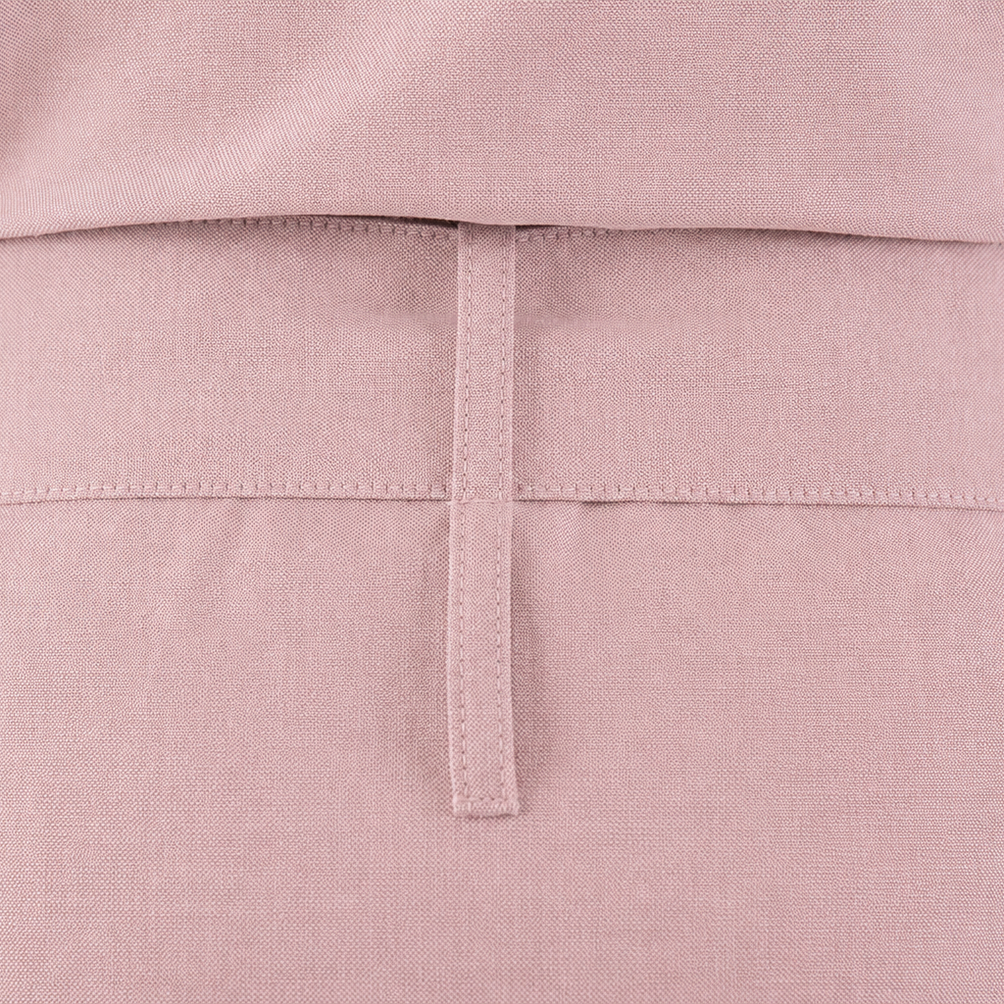 Close-up of a dusty pink garment showing the back waistband with a vertical stitched tab detail.