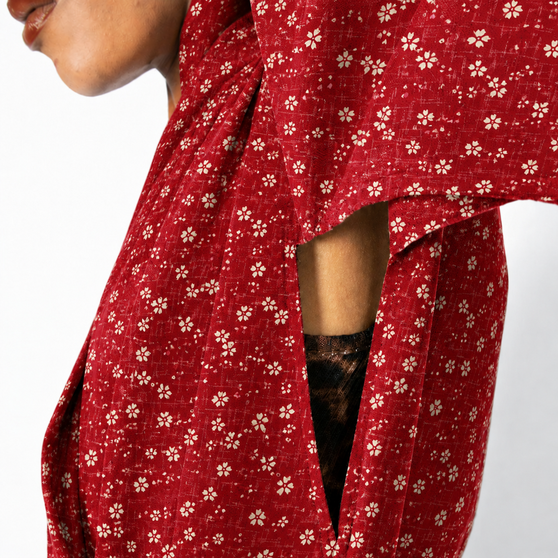 Close-up of a person wearing a red wrap-style garment with a small white floral print, showing part of the face, arm, and the fabric drape against a plain light background.