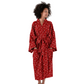 A woman wearing a red patterned bathrobe stands against a plain white studio background, looking to the side.
