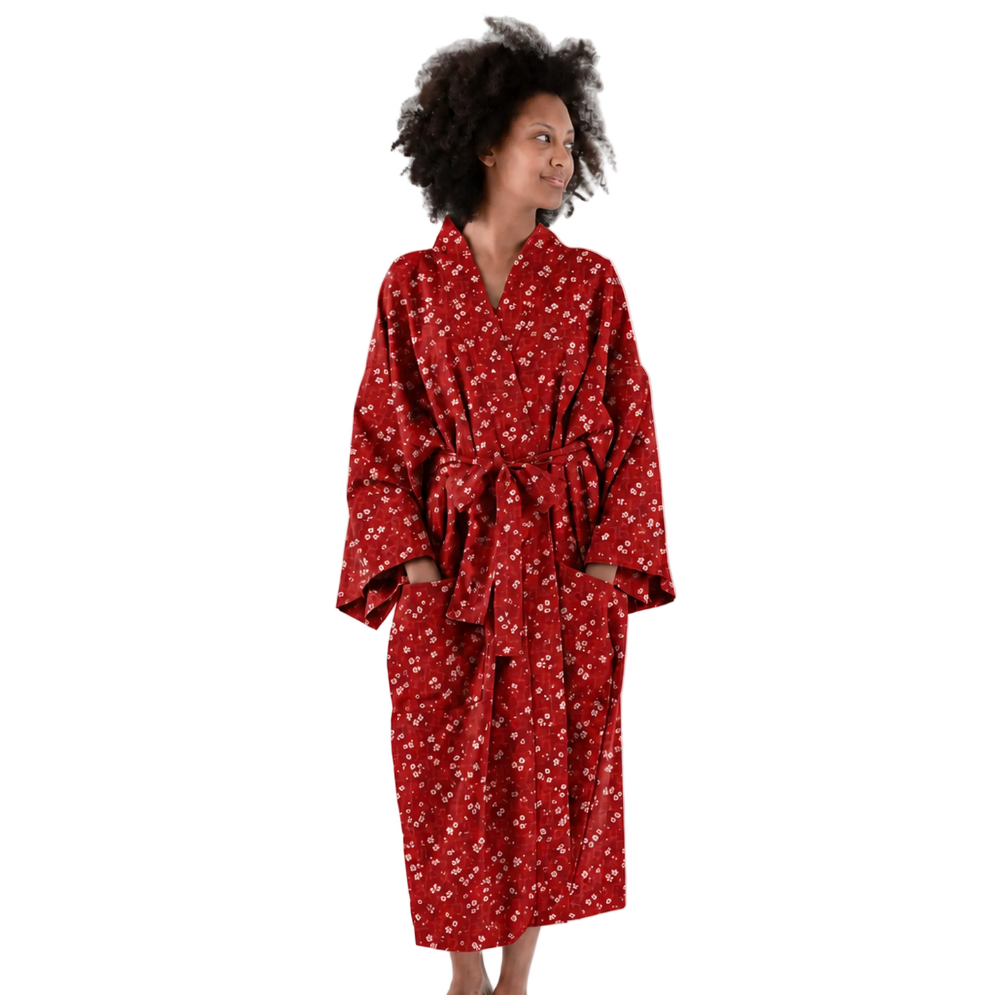 A woman wearing a red patterned bathrobe stands against a plain white studio background, looking to the side.