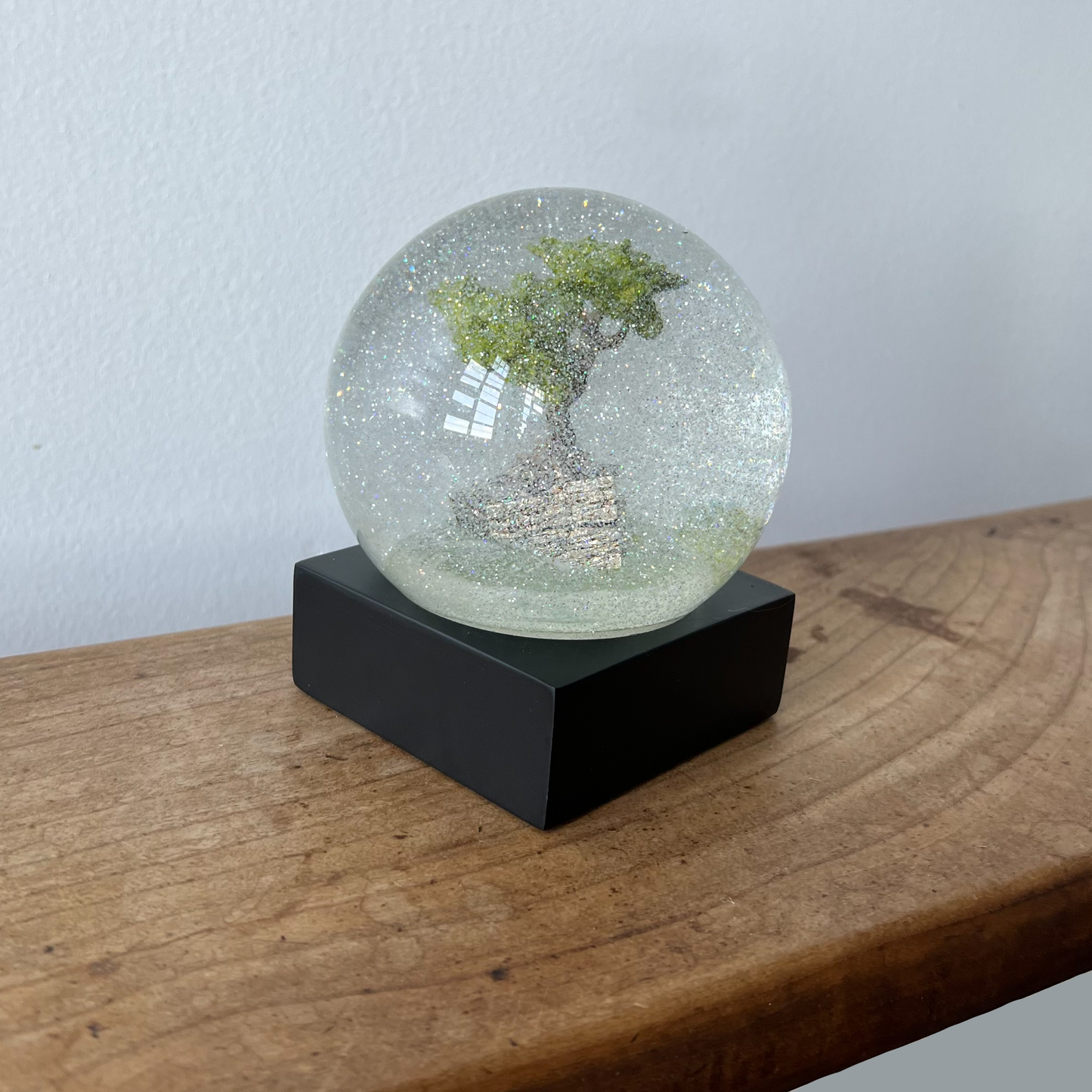 Bonsai tree snow globe on wooden ledge with snow flurrying